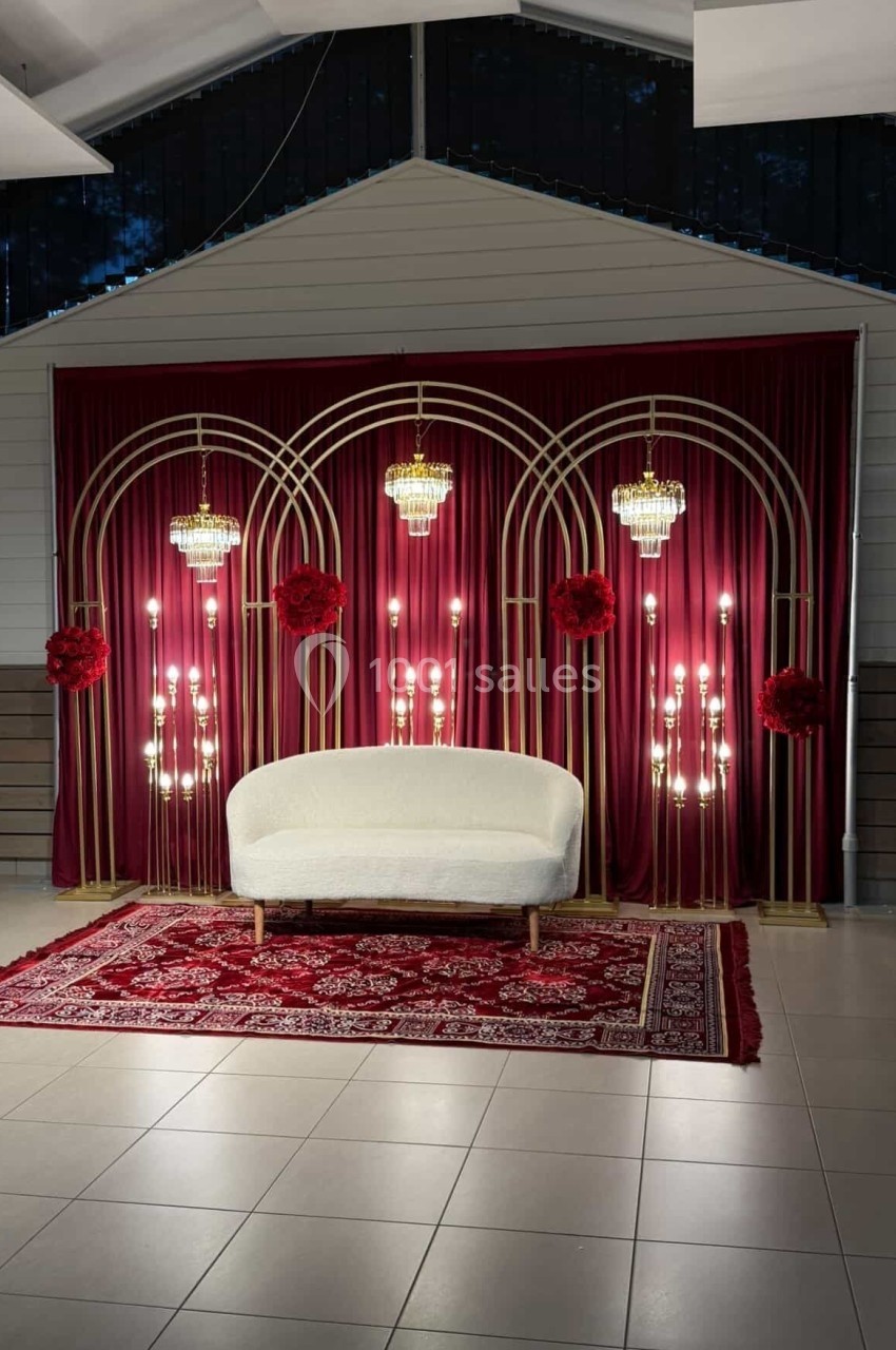 Canapé blanc devant un décor avec rideaux rouges, arches dorées, lustres et tapis rouge à motifs.