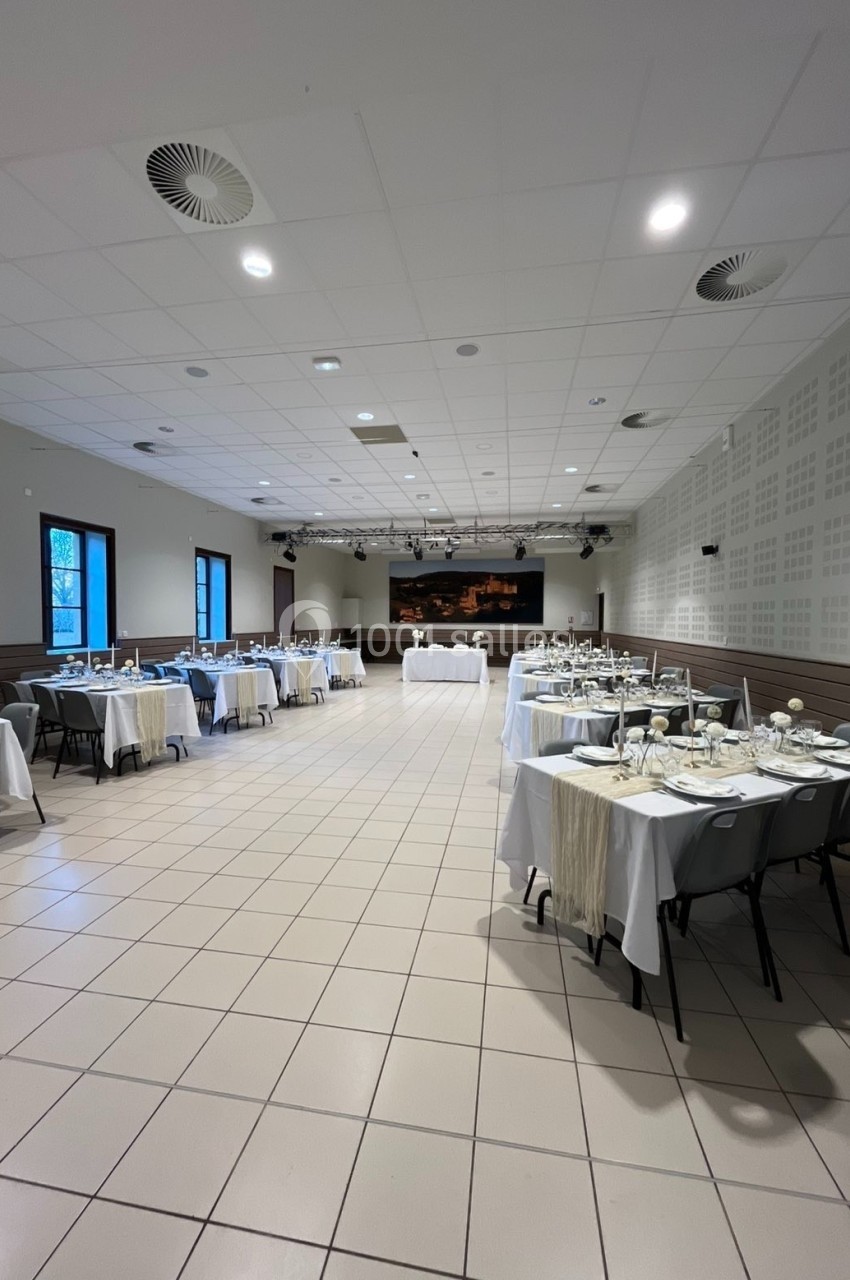 Salle de réception lumineuse avec tables dressées pour un événement, nappes blanches et décoration sobre.