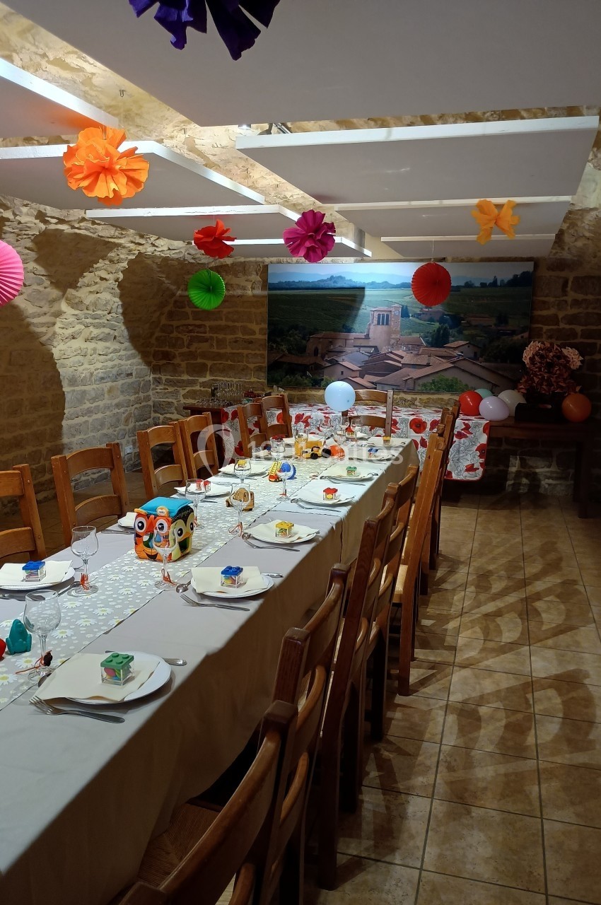 Table dressée pour un repas festif dans une salle en pierre, décorée de guirlandes et lanternes colorées.