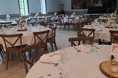 Salle de réception avec tables dressées, décorées de feuillages et vaisselle, éclairée par de grandes baies vitrées.