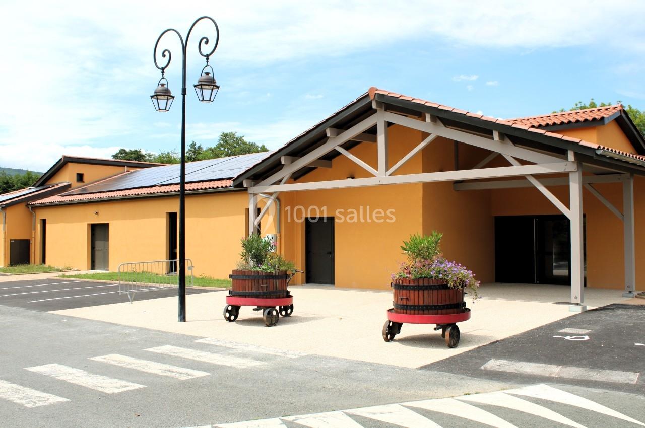 Bâtiment moderne à façade orange avec toit en tuiles, lampadaire et jardinières en tonneaux devant l'entrée.
