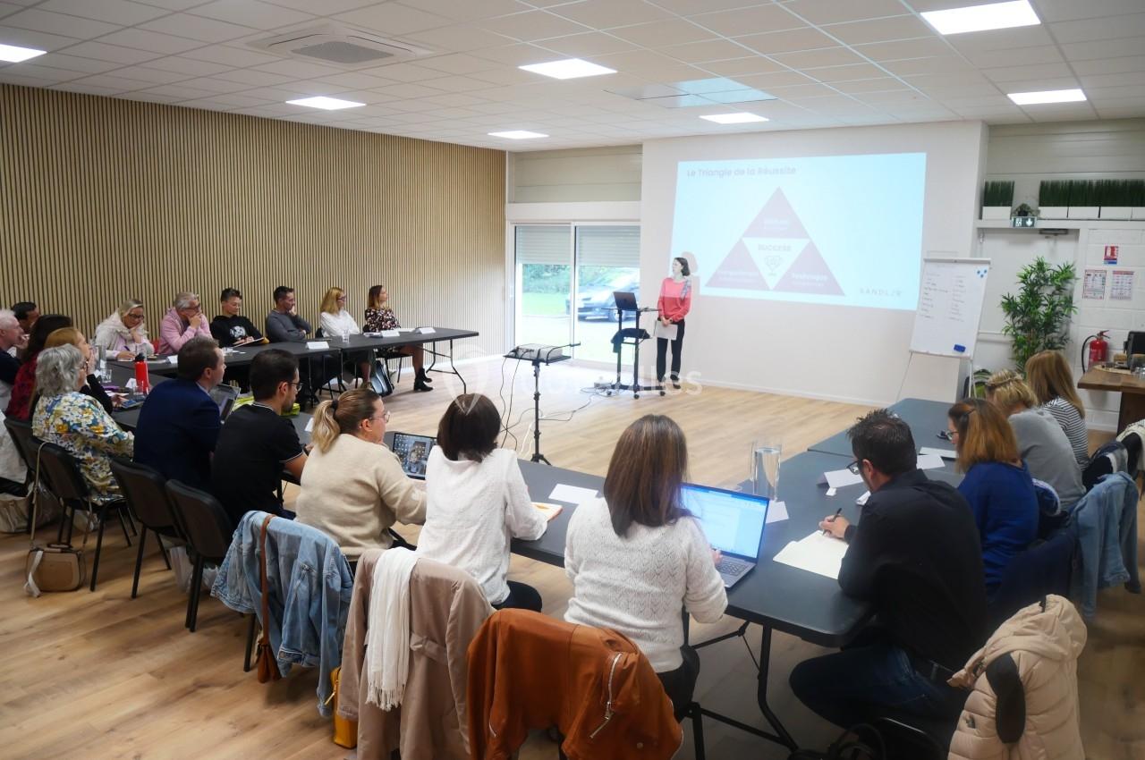 Une formatrice présente un diaporama à un groupe de personnes assises autour de tables dans une salle de réunion.