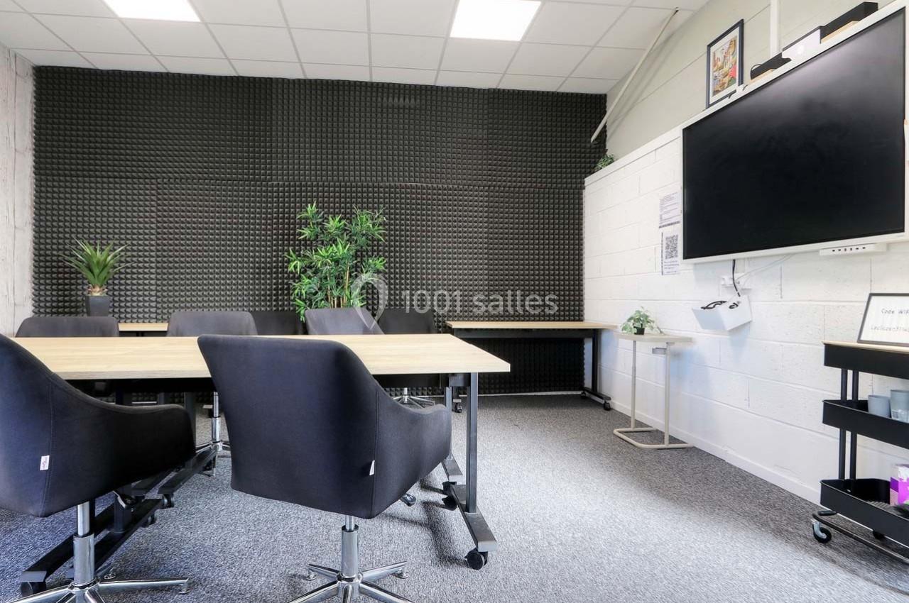 Salle de réunion moderne avec table en bois, chaises noires, mur insonorisé et écran mural.