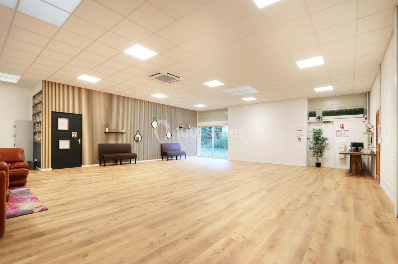 Salle spacieuse avec parquet clair, murs décorés, canapés, étagères et grandes baies vitrées donnant sur un espace vert.