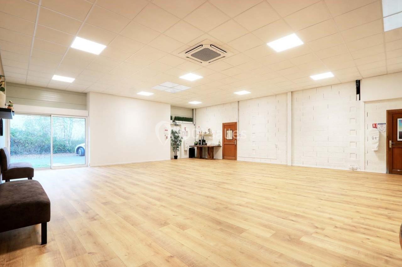 Salle spacieuse avec parquet clair, murs blancs, éclairage au plafond et grande baie vitrée donnant sur l'extérieur.