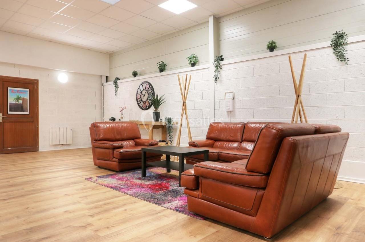 Salon avec canapés en cuir marron, table basse noire, tapis coloré et plantes décoratives dans un espace lumineux.
