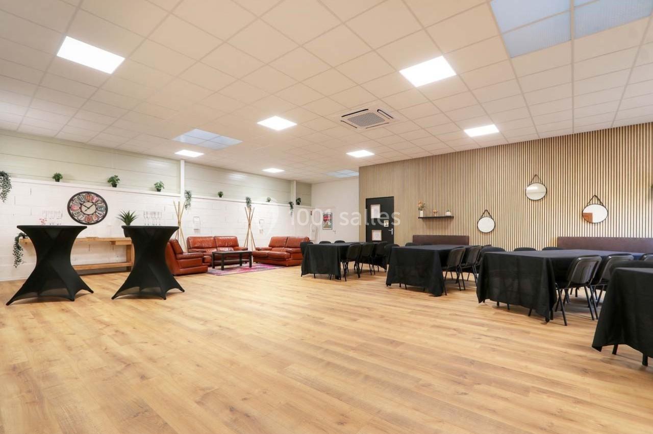 Salle lumineuse avec parquet, tables noires, canapés en cuir, décorations murales et plantes suspendues.