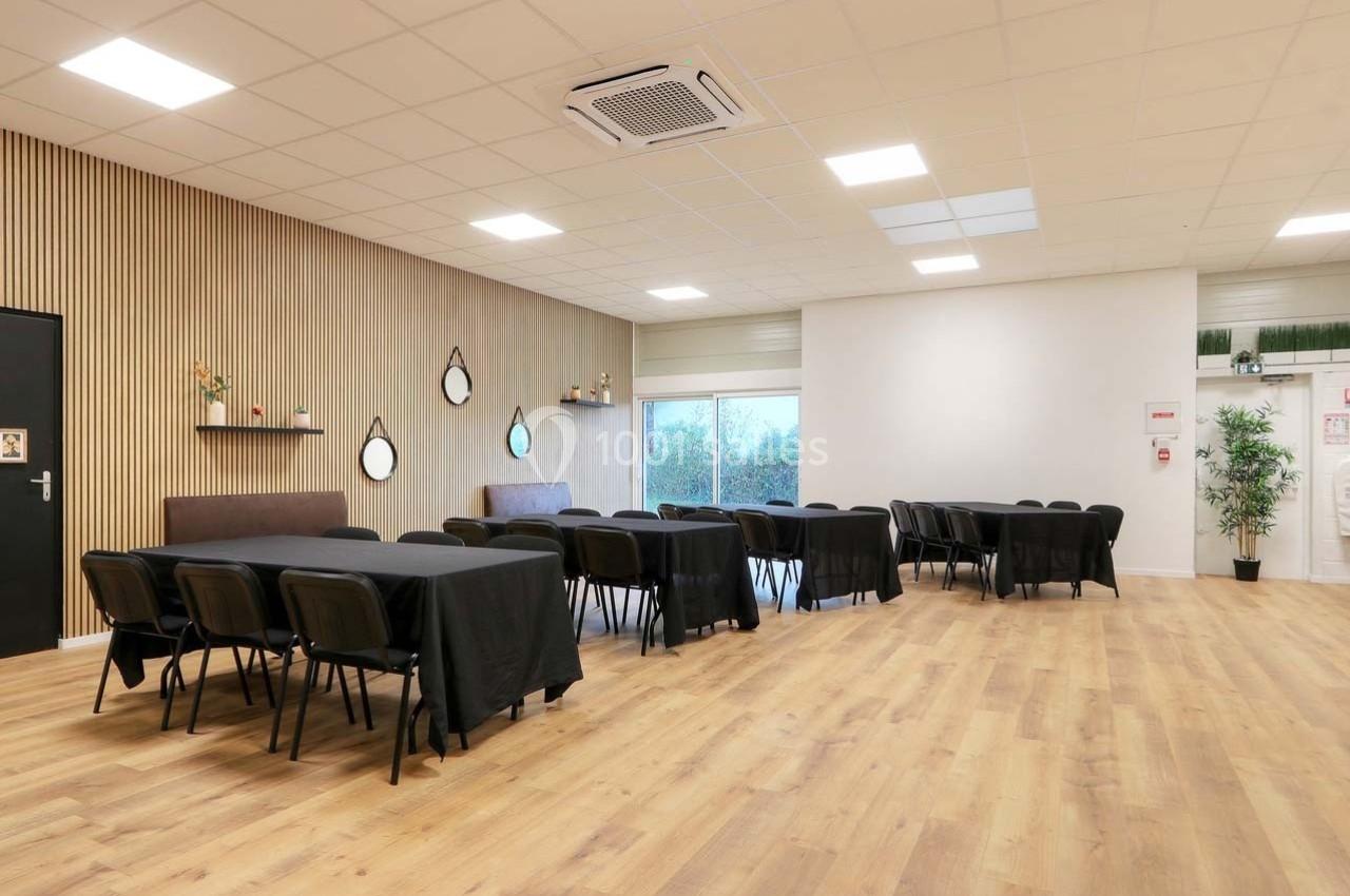 Salle lumineuse avec parquet, tables noires alignées, chaises, murs clairs et décorations murales minimalistes.