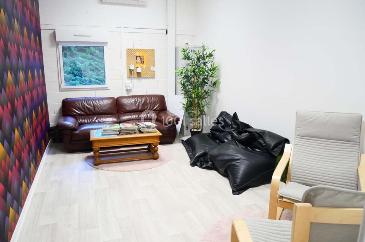 Salon lumineux avec canapé en cuir, poufs noirs, fauteuils en bois, table basse et mur décoratif coloré.