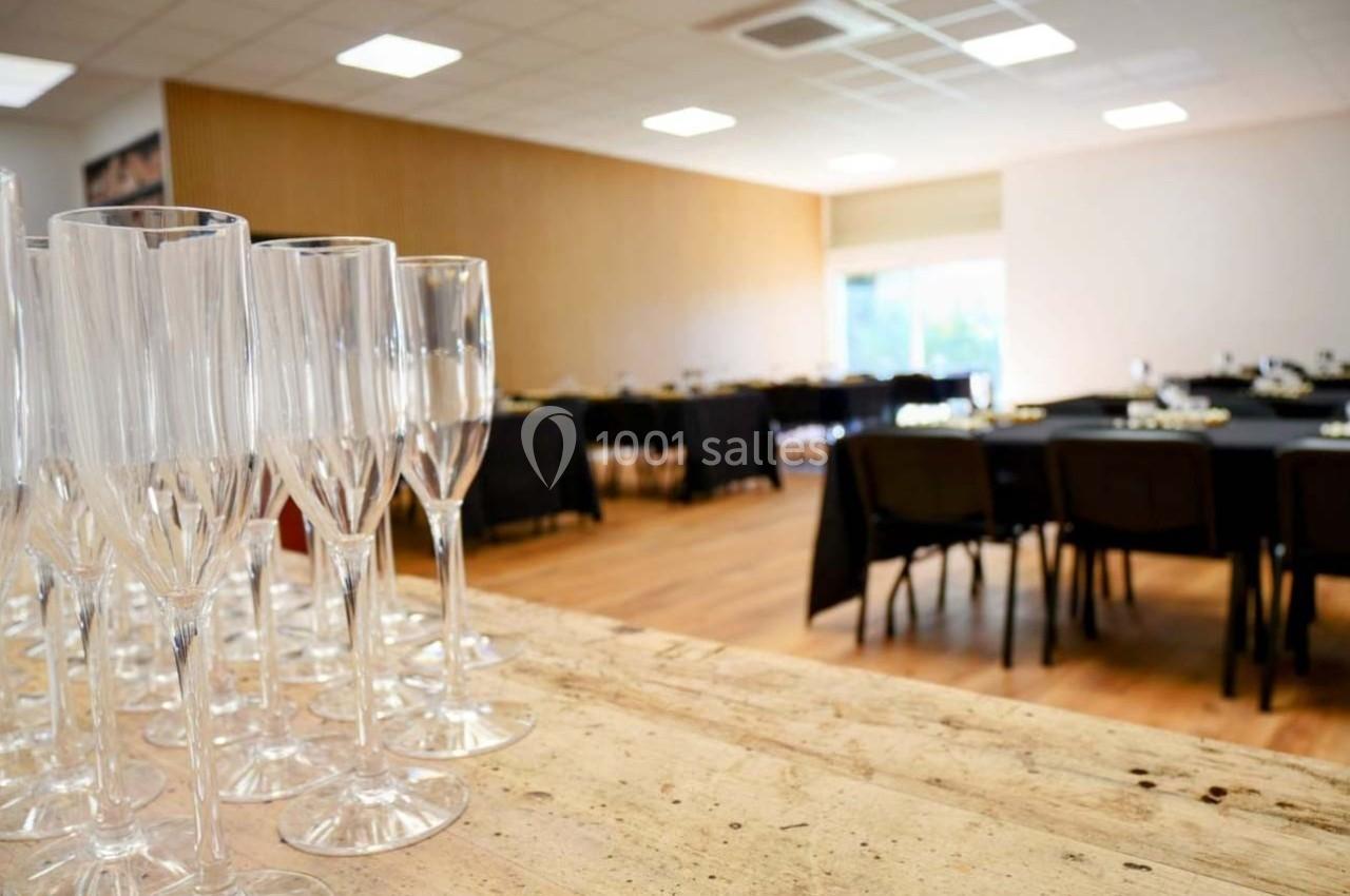 Verres à champagne alignés sur une table en bois, avec une salle de réception aménagée en arrière-plan.