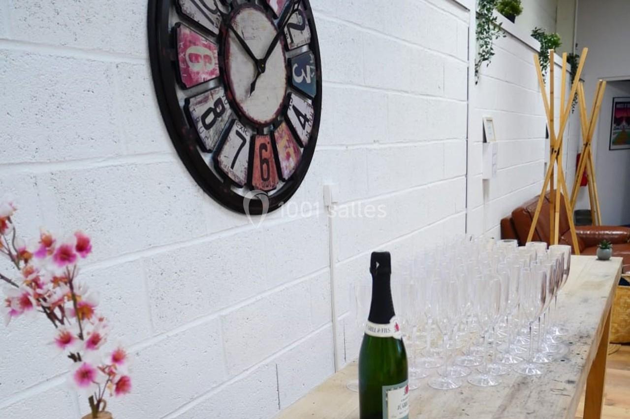 Bouteille de champagne et rangée de flûtes sur une table en bois, avec une horloge murale en arrière-plan.