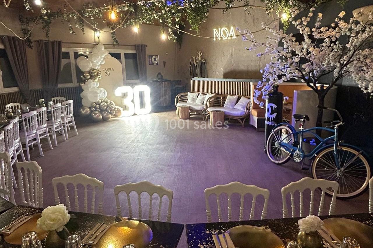 Salle décorée pour une fête avec des tables dressées, un grand ’30’ lumineux, des ballons et un vélo en arrière-plan.