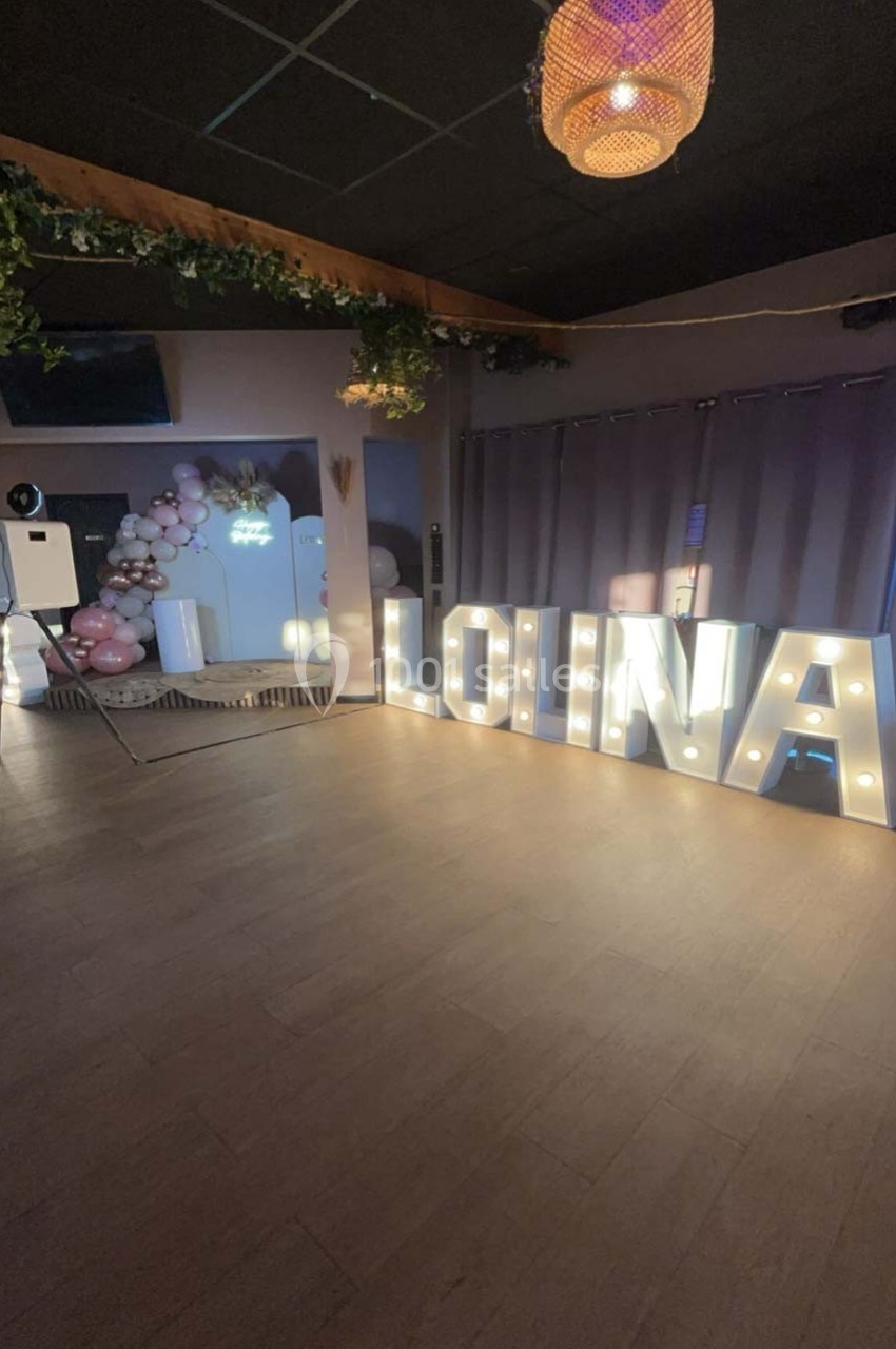 Lettres lumineuses formant ’Lolita’ dans une salle décorée avec des ballons roses et blancs, ambiance festive.