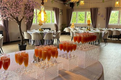 Salle de réception décorée avec des tables dressées et un buffet de cocktails sur une nappe blanche.