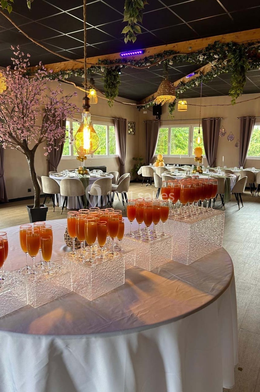 Salle de réception décorée avec des tables dressées et un buffet de cocktails sur une nappe blanche.