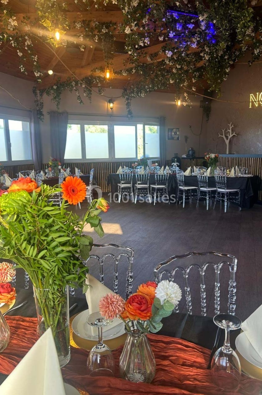 Salle décorée pour un événement avec tables dressées, chaises transparentes et fleurs colorées en centre de table.