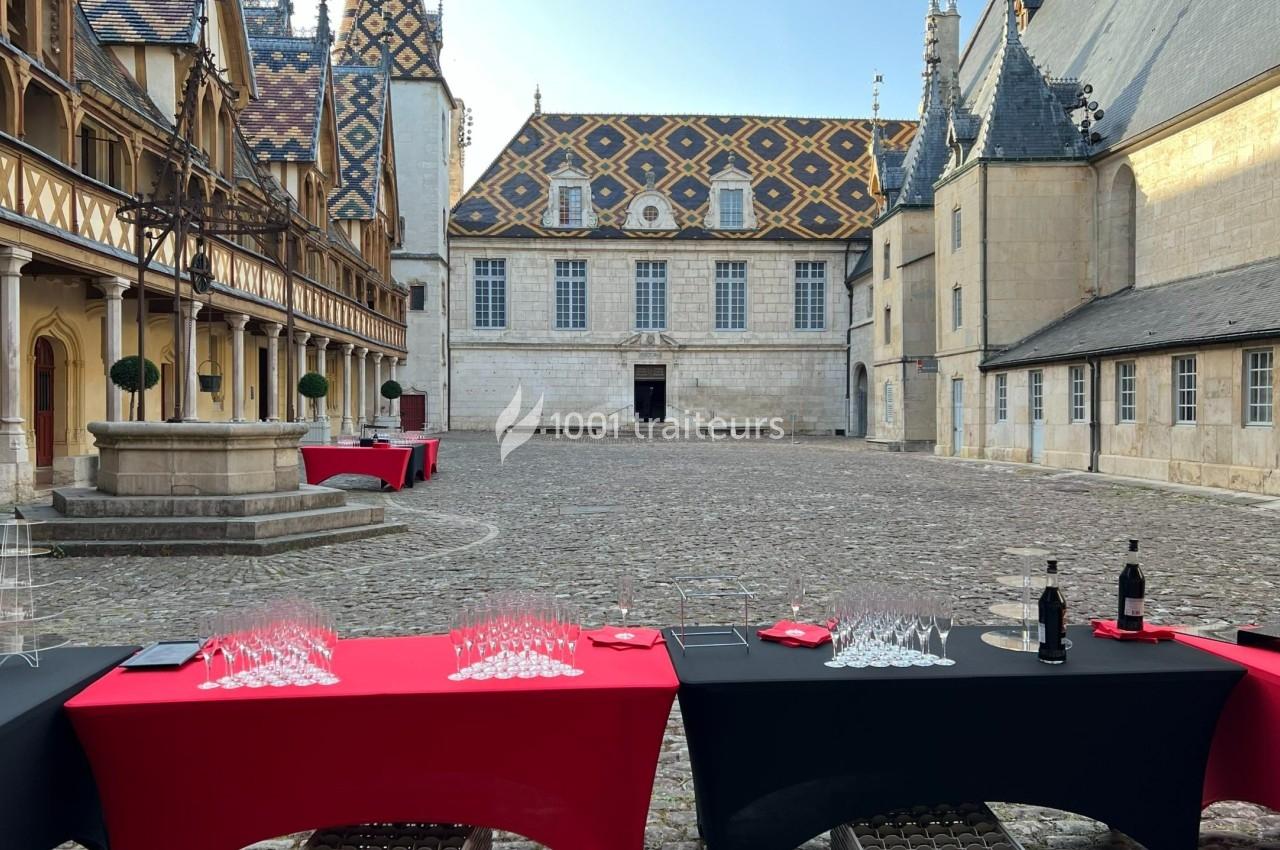 Cour intérieure pavée avec tables dressées pour un événement, entourée de bâtiments historiques aux toits colorés.