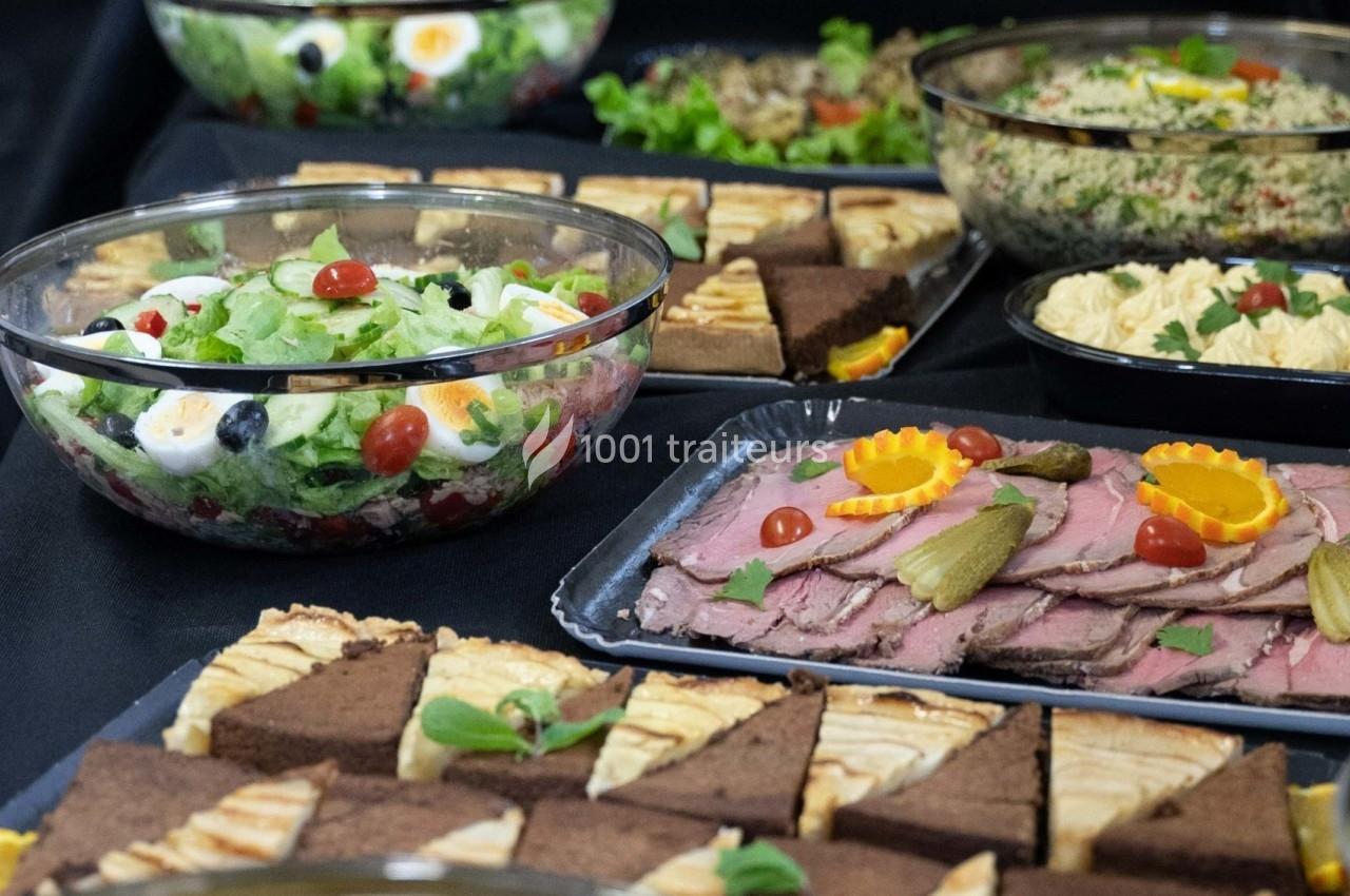 Buffet composé de salades, tranches de rôti garnies, parts de gâteaux et autres plats variés sur une nappe noire.