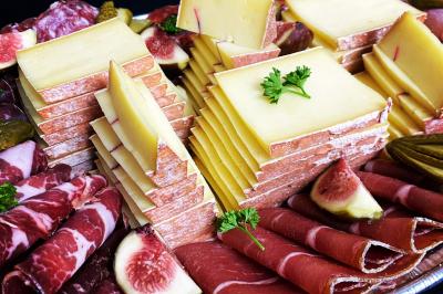 Plateau de charcuterie avec jambon, saucisson, cornichons, tomates cerises et feuilles de salade en décoration.