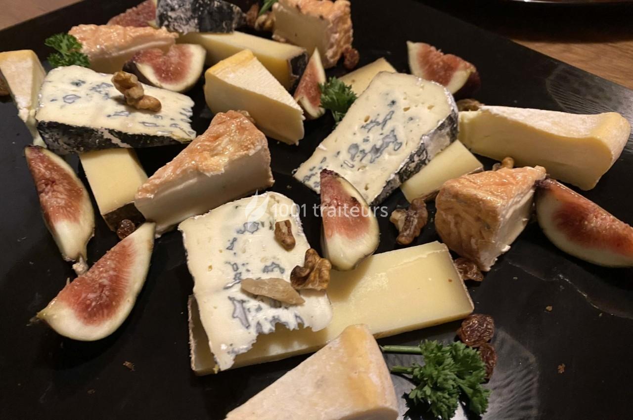Assortiment de fromages variés avec morceaux de figues fraîches, noix et raisins secs sur un plateau noir.