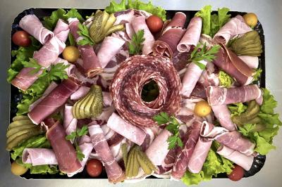 Plateau de charcuterie avec jambon, saucisson, cornichons, tomates cerises et feuilles de salade en décoration.