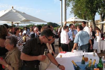 Un groupe de personnes échange autour d'un buffet en plein air, avec des serveurs et un paysage de vignoble en arrière-plan.