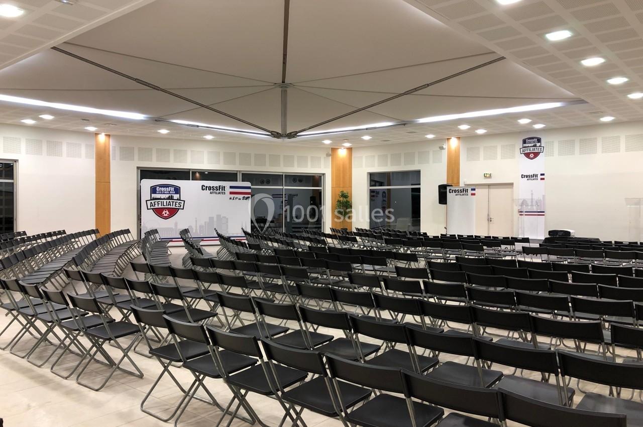 Salle de conférence avec rangées de chaises noires vides, affiches et panneaux CrossFit en arrière-plan.