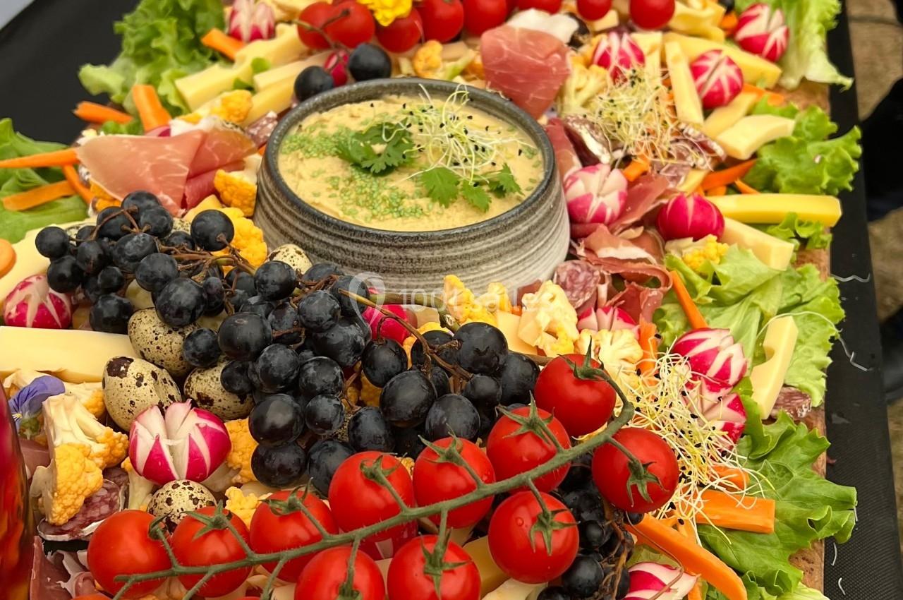 Plateau coloré de charcuteries, fromages, légumes frais et fruits, disposés autour d'une sauce au centre.
