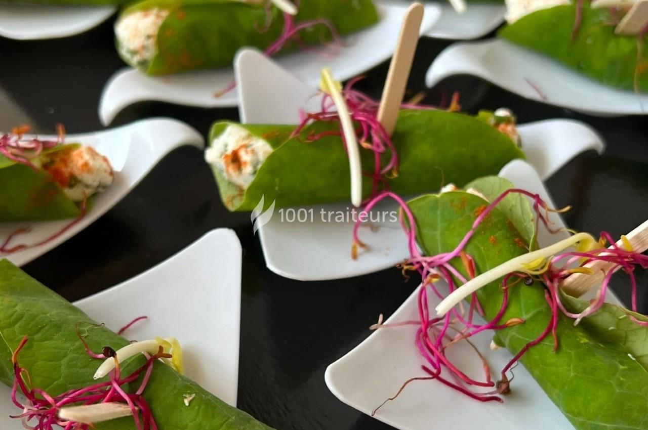Rouleaux de feuilles vertes garnis de fromage frais, décorés de pousses roses et présentés sur des assiettes individuelles…