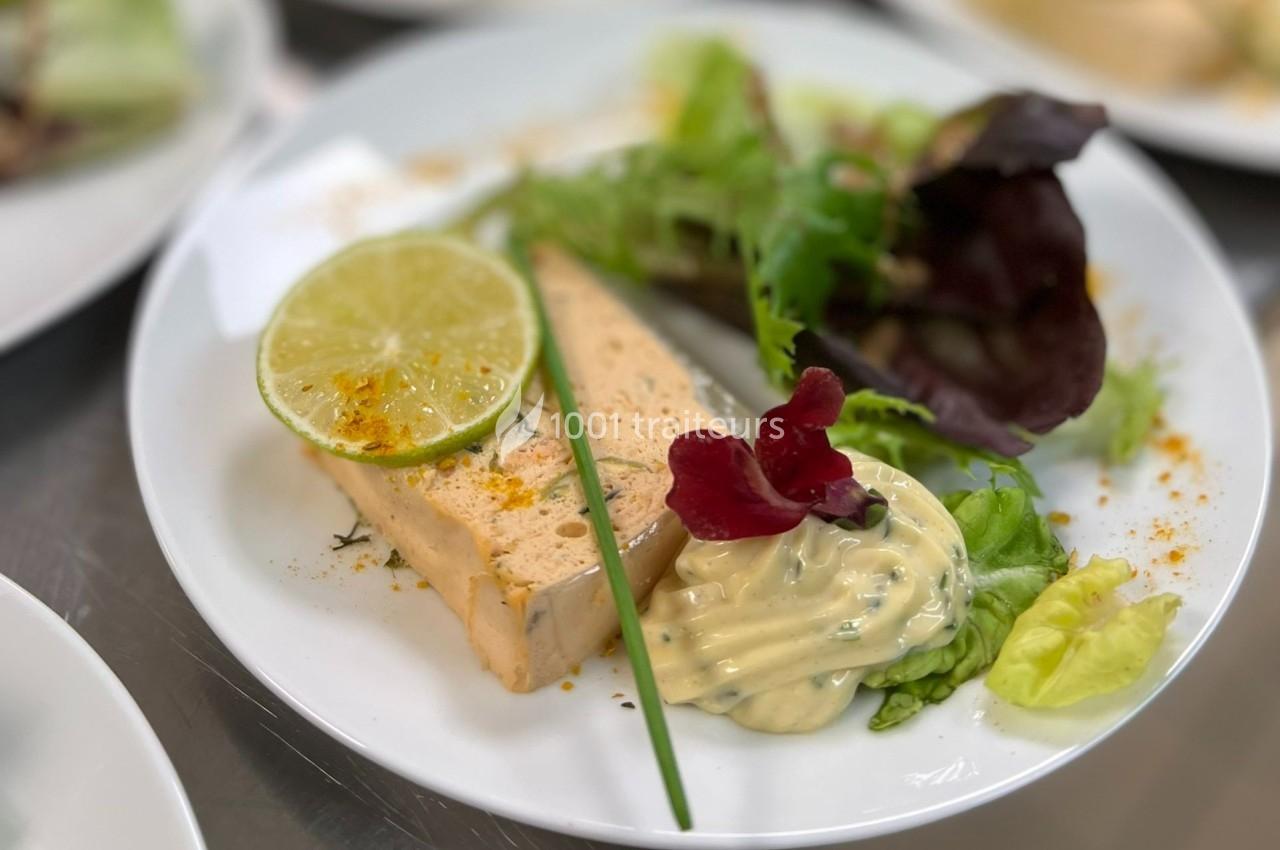 Assiette contenant une tranche de terrine, une rondelle de citron vert, de la salade verte et une sauce crémeuse.