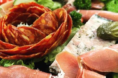 Plateau de charcuterie avec jambon, saucisson, cornichons, tomates cerises et feuilles de salade en décoration.