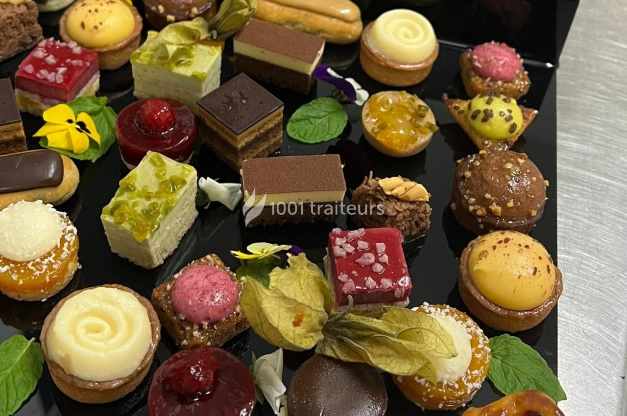 Plateau de mignardises variées comprenant tartelettes, éclairs, gâteaux et décorations florales sur fond noir.