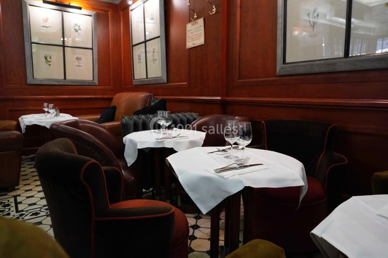 Salle de restaurant avec tables dressées, nappes blanches, fauteuils en velours et boiseries murales.