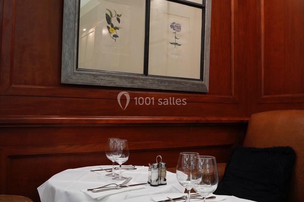 Deux tables dressées avec nappes blanches dans un restaurant aux murs en bois, décorées de cadres avec illustrations…