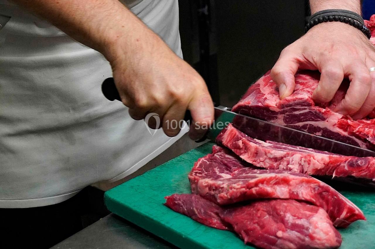 Un boucher tranche des morceaux de viande rouge sur une planche à découper verte.