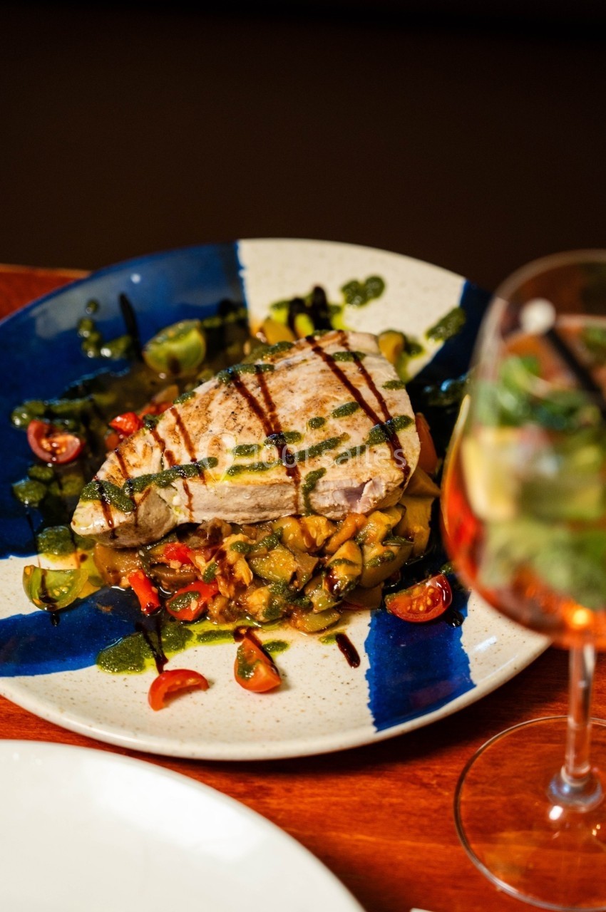 Assiette de thon grillé accompagné de légumes colorés et de sauce verte, servie sur une table en bois.