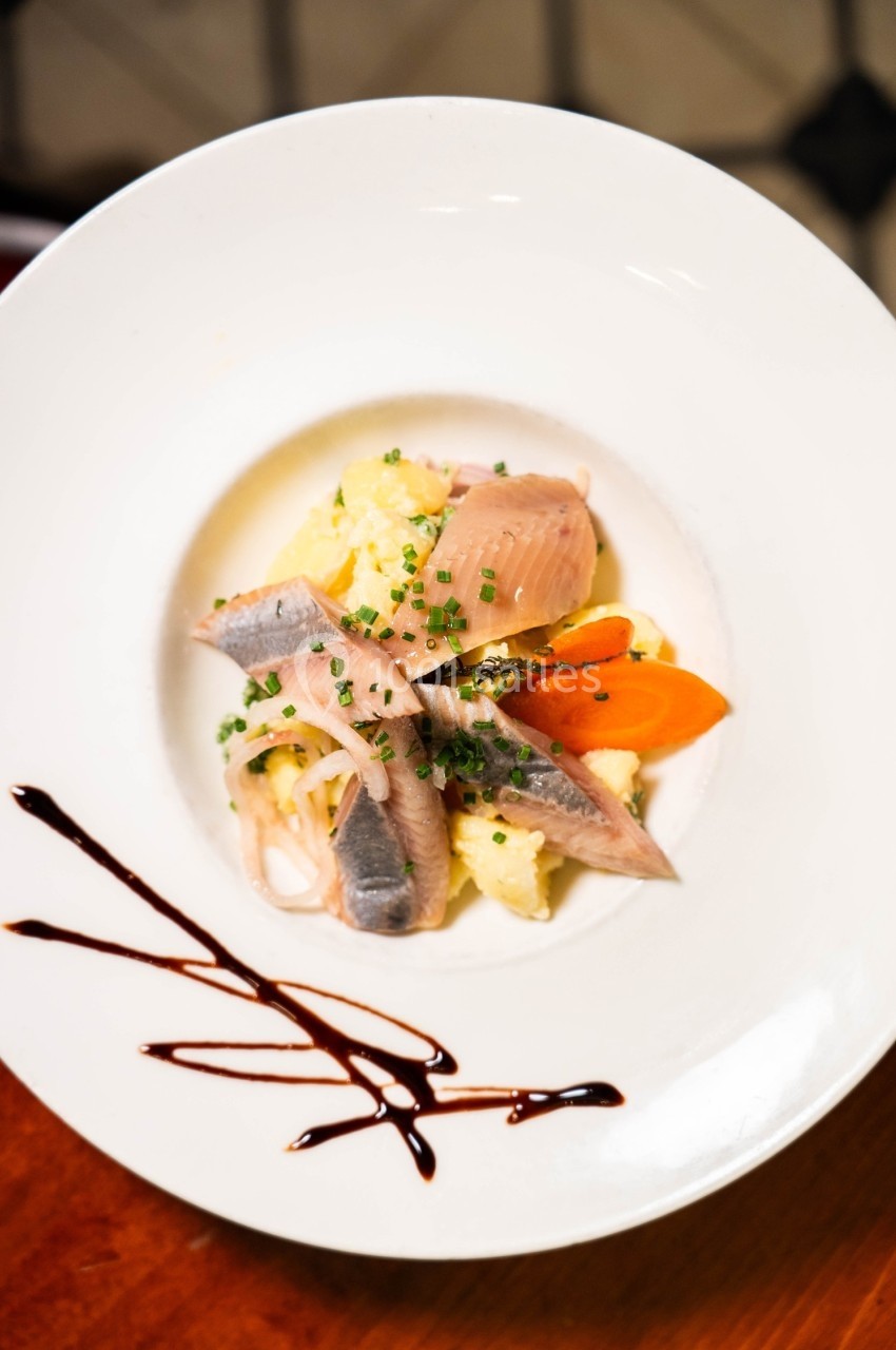 Assiette de hareng mariné avec pommes de terre, carottes et ciboulette, décorée de traits de sauce balsamique.