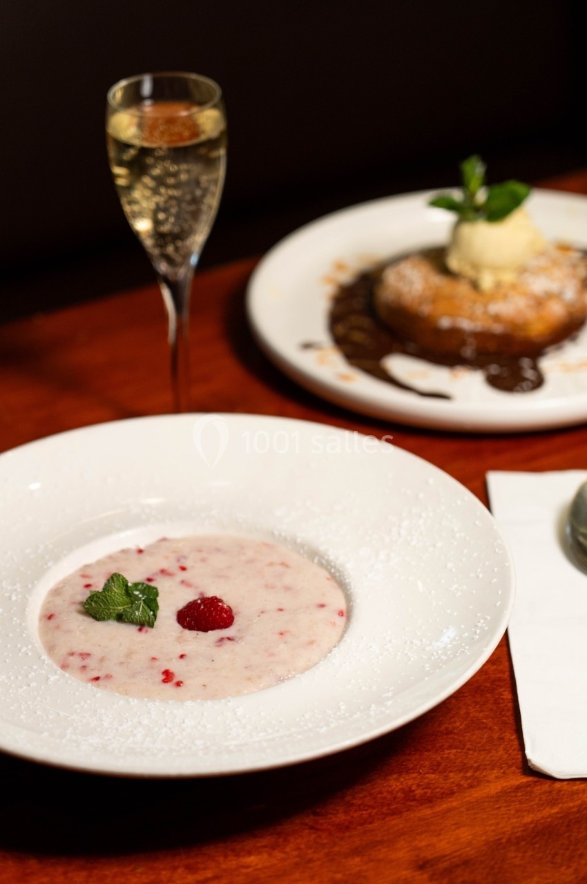 Un dessert crémeux aux framboises dans une assiette blanche, accompagné d'un verre de champagne et d'un autre dessert au…
