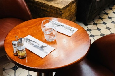 Table ronde en bois avec deux couverts, un verre d'eau et des condiments, entourée de fauteuils en cuir marron.