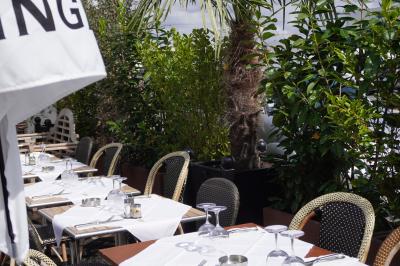 Terrasse extérieure avec tables dressées, nappes blanches, chaises en osier et végétation luxuriante en arrière-plan.