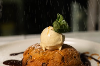 Un dessert crémeux garni de framboises et de menthe, avec un gâteau et une coupe de champagne en arrière-plan.