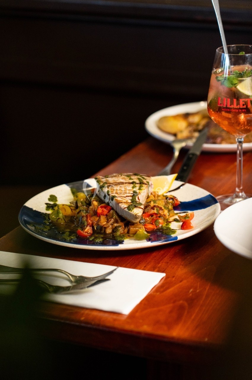 Assiette de thon grillé accompagné de légumes colorés, servie sur une table en bois avec un verre de cocktail.