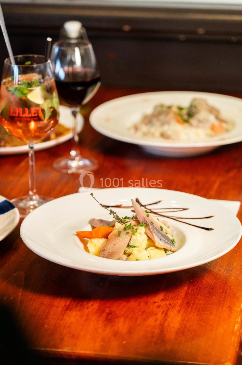 Assiette de poisson fumé avec légumes et sauce, servie sur une table en bois avec des verres de vin en arrière-plan.
