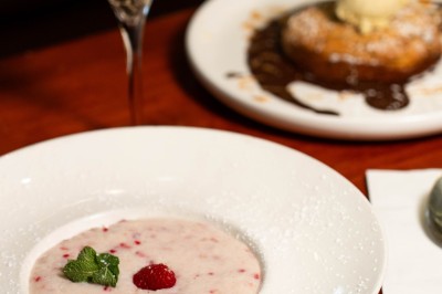 Un dessert crémeux garni de framboises et de menthe, avec un gâteau et une coupe de champagne en arrière-plan.