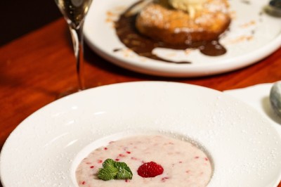 Un dessert crémeux garni de framboises et de menthe, avec un gâteau et une coupe de champagne en arrière-plan.