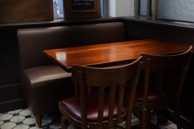 Salle de restaurant avec tables en bois, chaises assorties et grandes fenêtres laissant entrer la lumière naturelle.