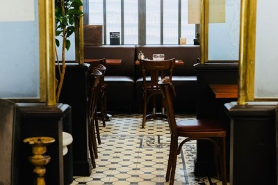 Salle de restaurant avec tables en bois, chaises assorties et grandes fenêtres laissant entrer la lumière naturelle.