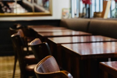Salle de restaurant avec tables en bois, chaises assorties et grandes fenêtres laissant entrer la lumière naturelle.