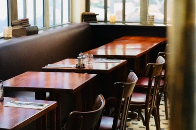 Salle de restaurant avec tables en bois, chaises assorties et grandes fenêtres laissant entrer la lumière naturelle.