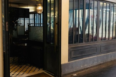 Salle de restaurant avec tables en bois, chaises assorties et grandes fenêtres laissant entrer la lumière naturelle.